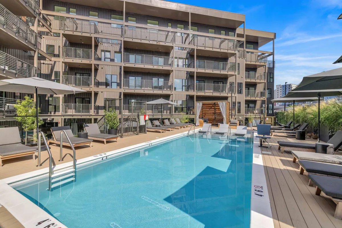 A stylish swimming pool area with lounging chairs, umbrella shades, and the facade of a modern building. The scene is set for sunbathing, socializing, and relaxing, evoking a resort-like atmosphere perfect for unwinding between city adventures.