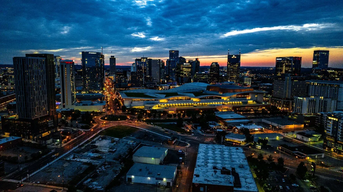 A vibrant view of Nashville's city skyline illuminated at night, with buildings aglow and a main roadway leading into the bustling urban core. The energy of the city is palpable, suggesting the proximity to nightlife, dining, and entertainment options.