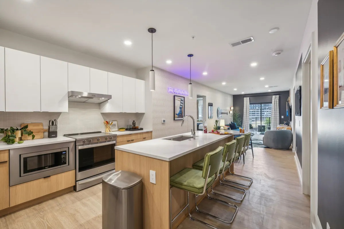 A vibrant, contemporary kitchen with a spacious island, modern appliances, bar stools, and decorative wall art. The open layout creates an inviting space for cooking, mingling, and entertaining guests, connecting seamlessly to the living and dining areas.