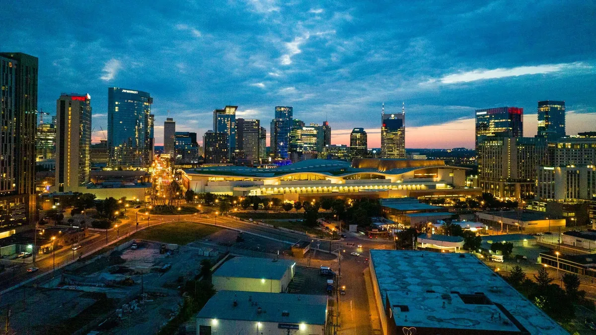 A stunning nighttime view of Nashville's city skyline, illuminated buildings, and the convention center. The city lights and urban landscape evoke the excitement and vibrancy of downtown, hinting at the music, events, and energetic atmosphere accessible to guests staying here.