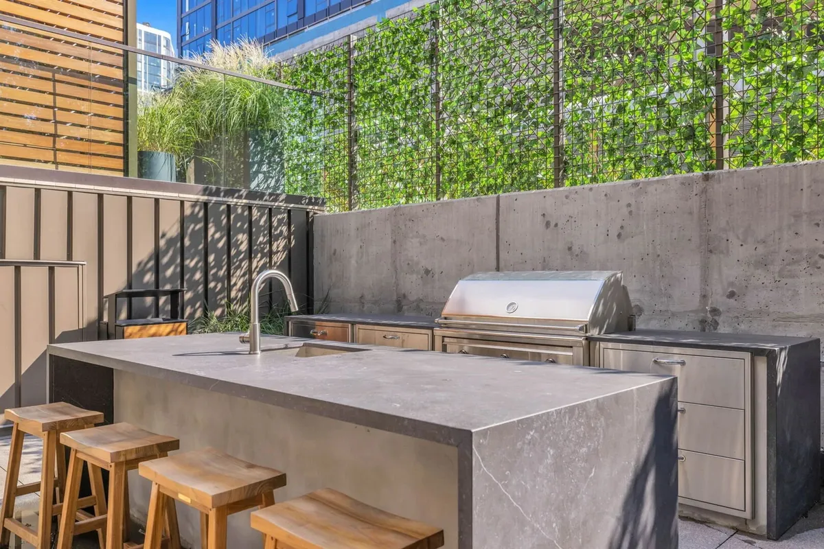 A dedicated outdoor grilling and kitchen space with a grill, bar stools, and a lush green wall, designed for casual outdoor dining and group celebrations. The setup is both inviting and functional, ready for BBQs and evening gatherings.